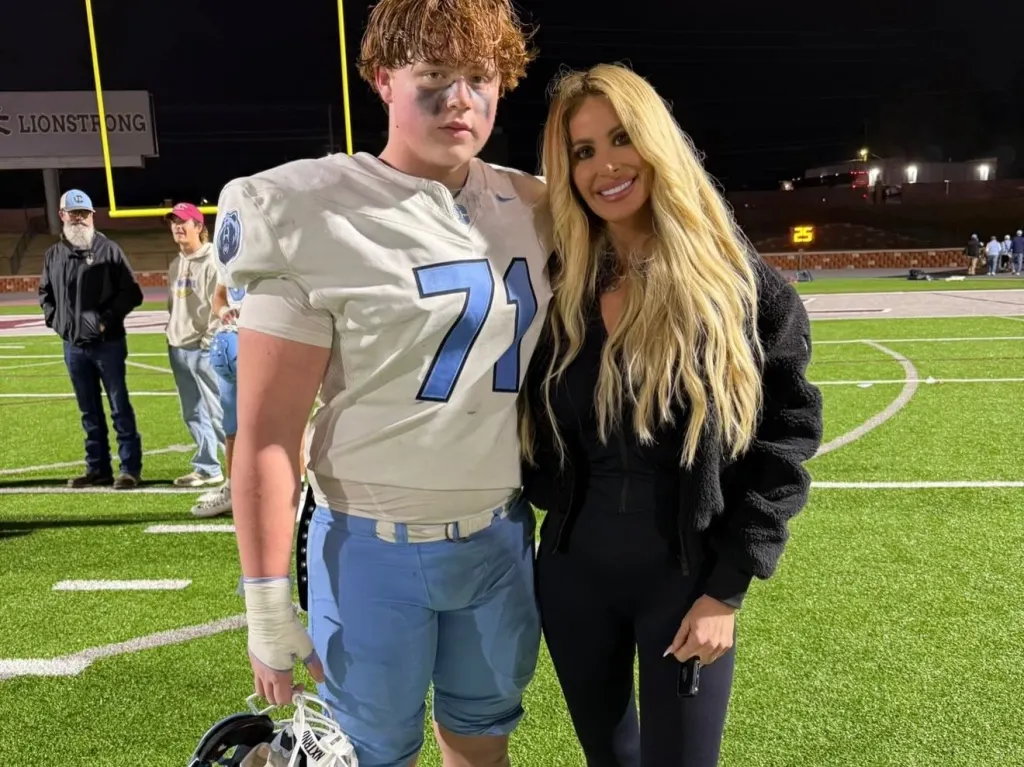 A young man in a football uniform and a woman with long blonde hair stand on a football field.