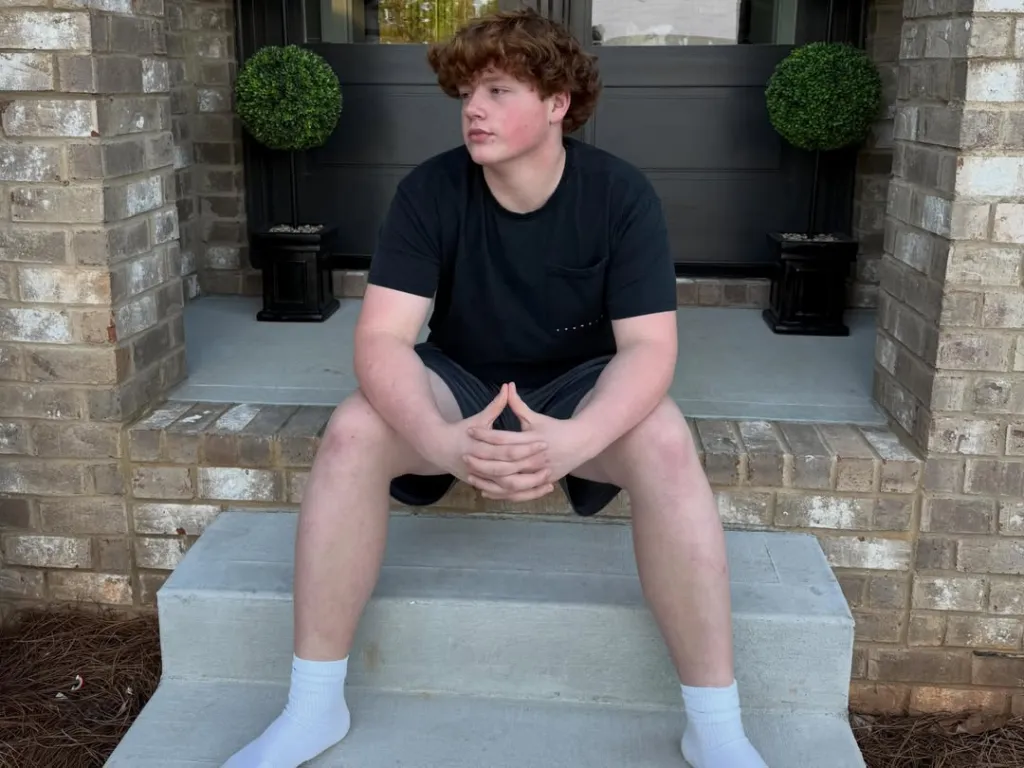 KJ Biermann sitting on a stoop outside a brick house.