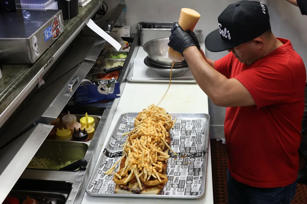 A kitchen crew member drizzles fat sauce onto a Fat Sal's Big Fat Fatty sandwich.