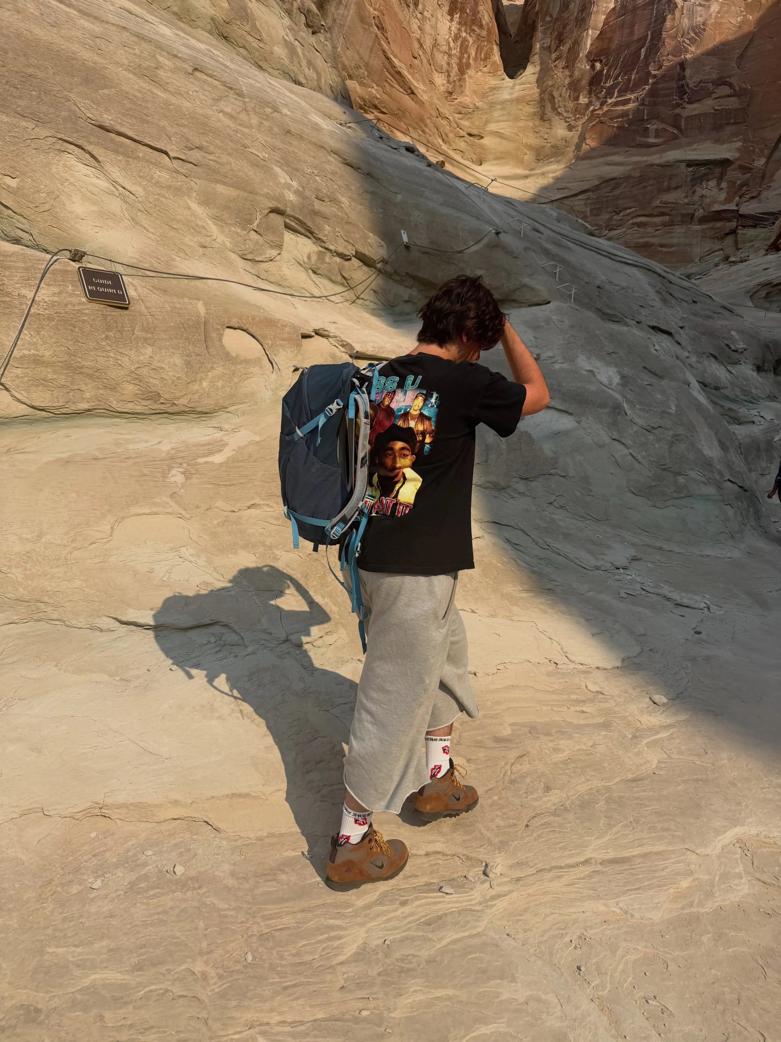 Mason Disick with a backpack hiking up a steep, rocky path with a 