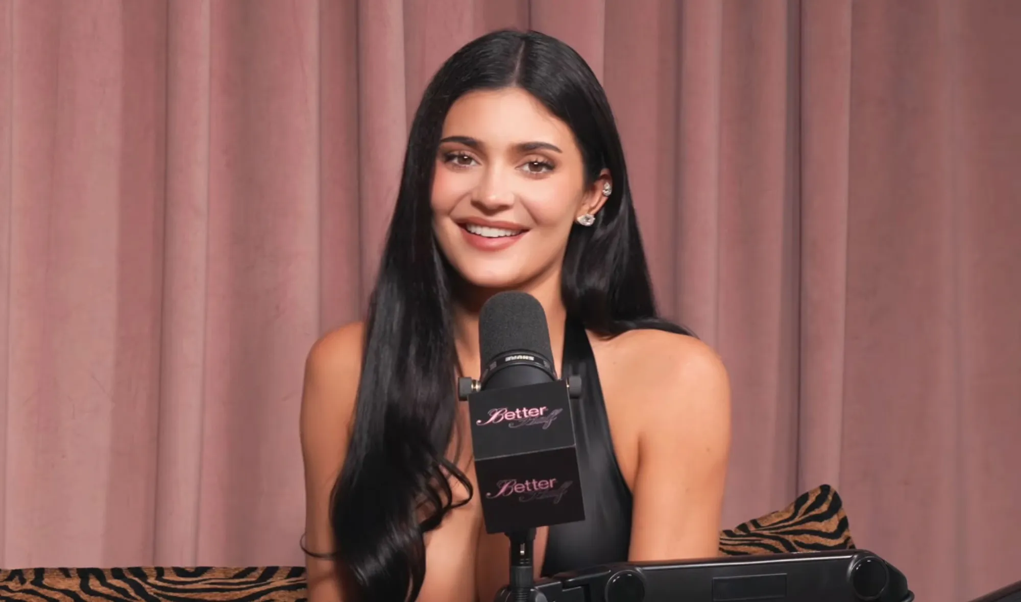 Kylie Jenner smiling while speaking into a podcast microphone with