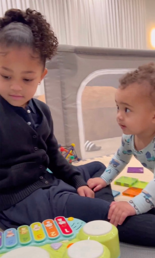 A young girl and toddler sit on the floor playing with toys.