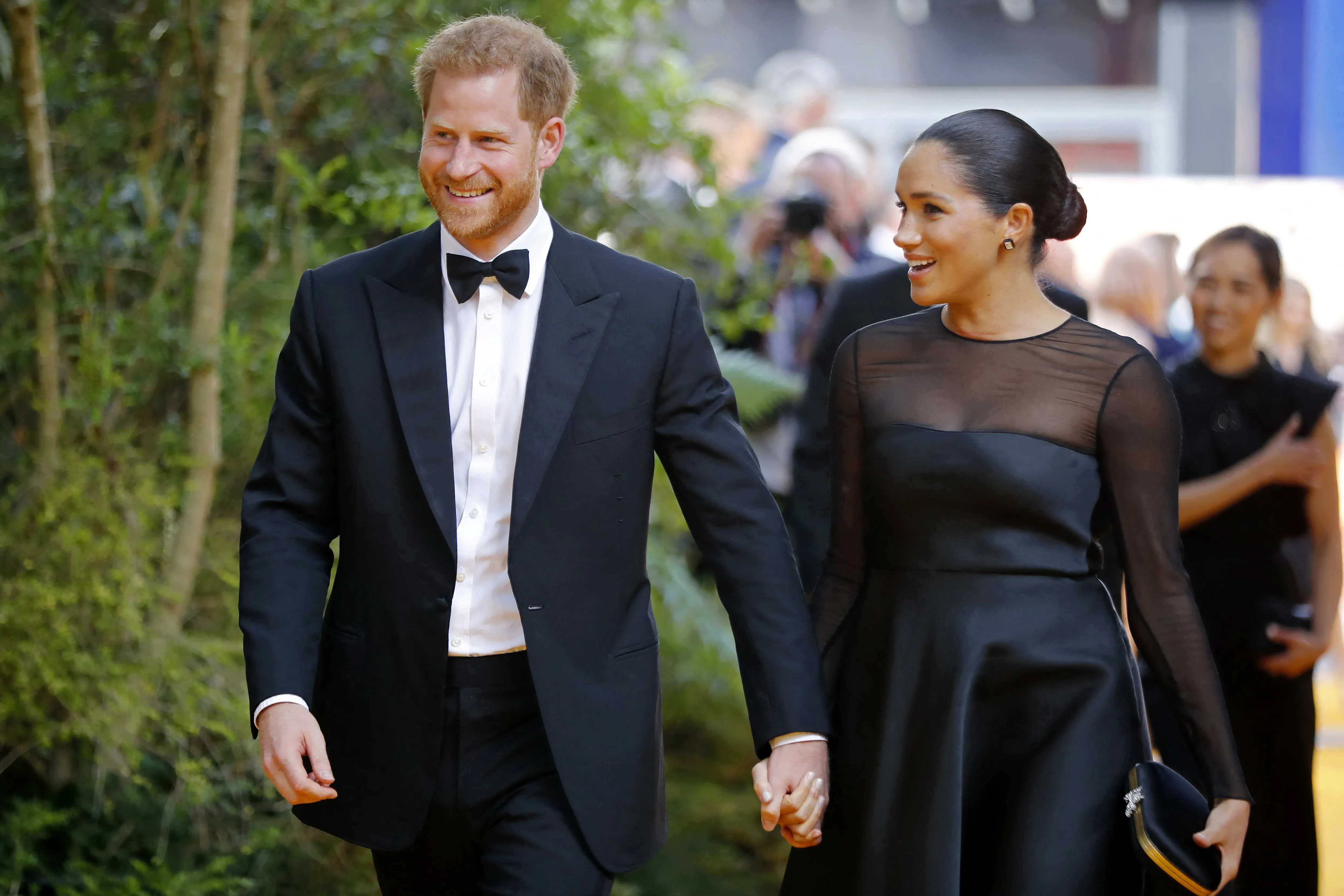Prince Harry and Meghan Markle holding hands while walking on a red carpet.
