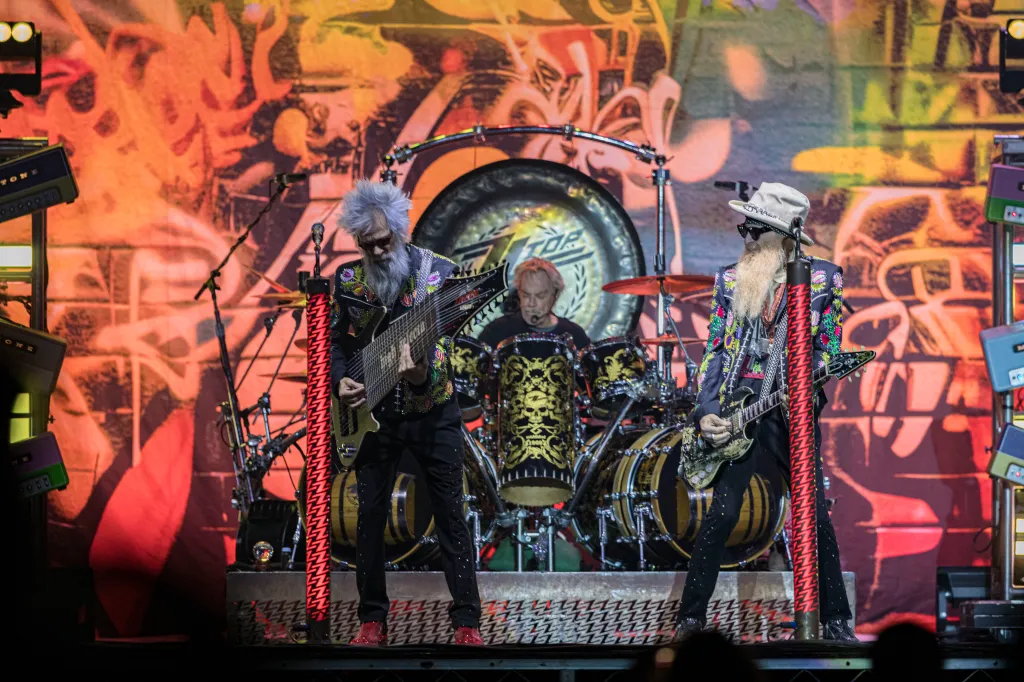 ZZ Top performing on stage, with Elwood Francis playing bass, Frank Beard on drums, and Billy Gibbons on guitar.