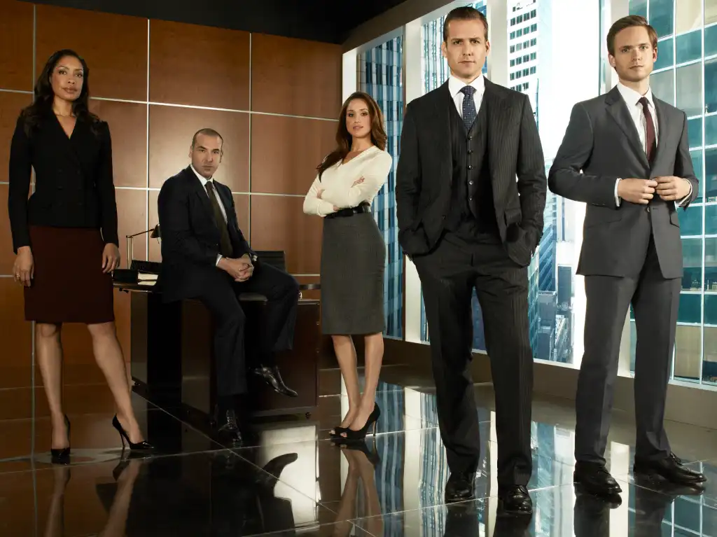 The cast of Suits: Gina Torres as Jessica, Rick Hoffman as Louis, Meghan Markle as Rachel Lane, Gabriel Macht as Harvey Specter, and Patrick Adams as Mike Ross.