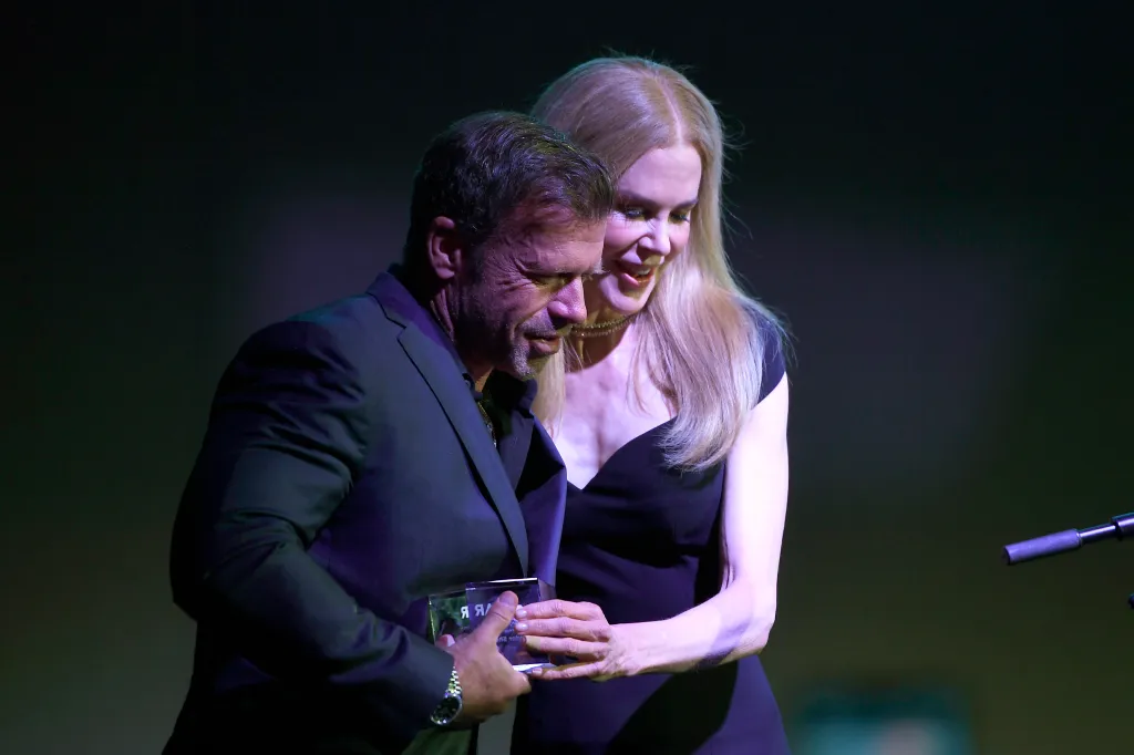 Taylor Sheridan, in a black suit, and Nicole Kidman, in a black dress, onstage with a clear award.