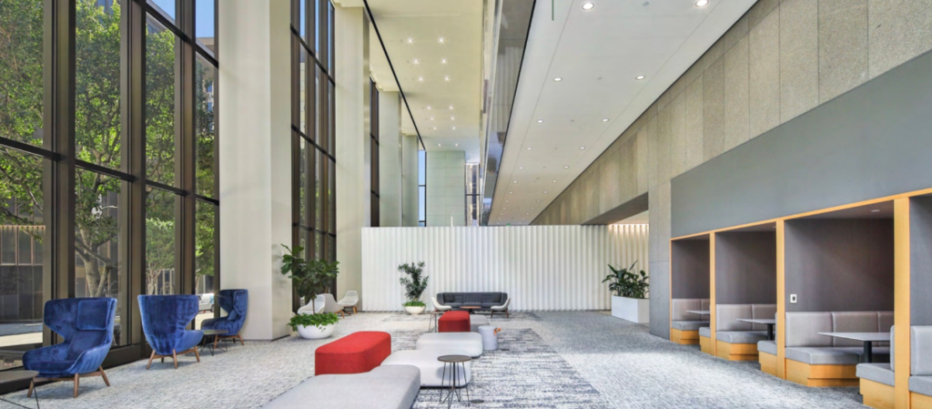 Luxurious lobby of the skyscraper where LAHSA operates, featuring floor-to-ceiling windows, blue velvet chairs, modern seating in red and white, and private booths.