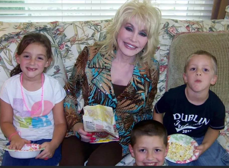 Dolly Parton on a couch with three young children, holding a bag of chips.