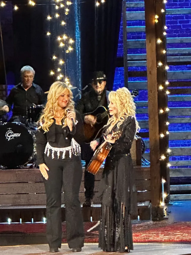 Dolly Parton on stage performing with a woman and two male musicians.