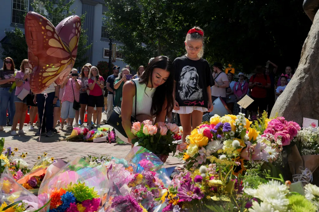 Lana Rezikova placing flowers at the Dolly Parton Statue with her daughter Sofia, who wears a Dolly Parton shirt, during a memorial gathering in Sevierville, Tennessee.