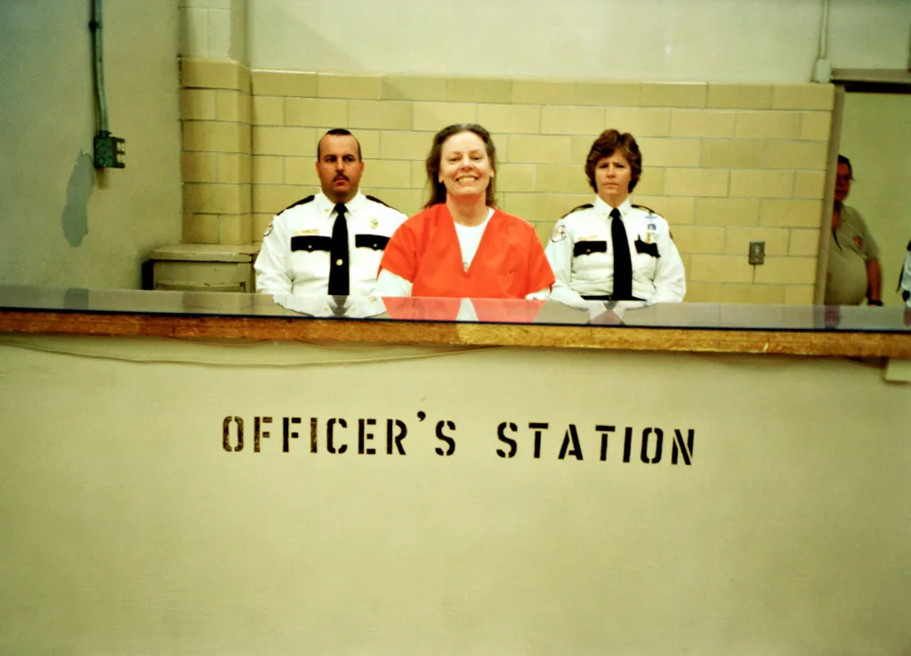 Aileen Wuornos smiling between two prison guards, filmed for *Aileen: Life and Death of a Serial Killer*.