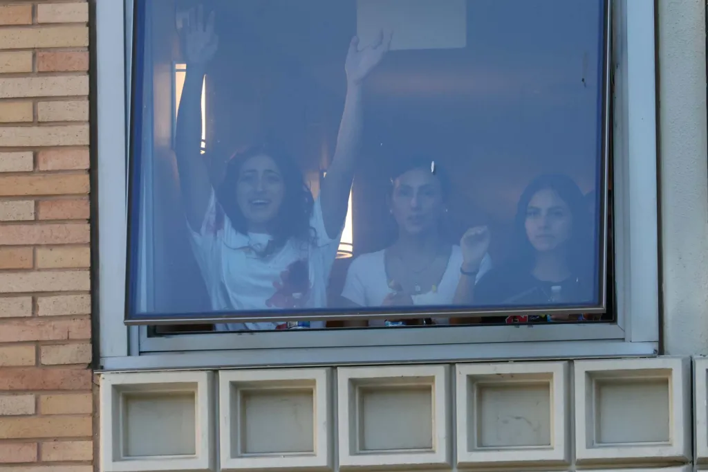 Three women look out a window, one with hands raised and another wearing a bloody shirt, during an LAPD SWAT drill at UCLA.