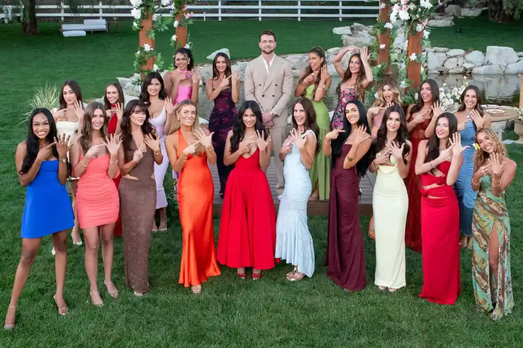 Twenty women, all wearing rings, pose around a man in a suit in a garden.
