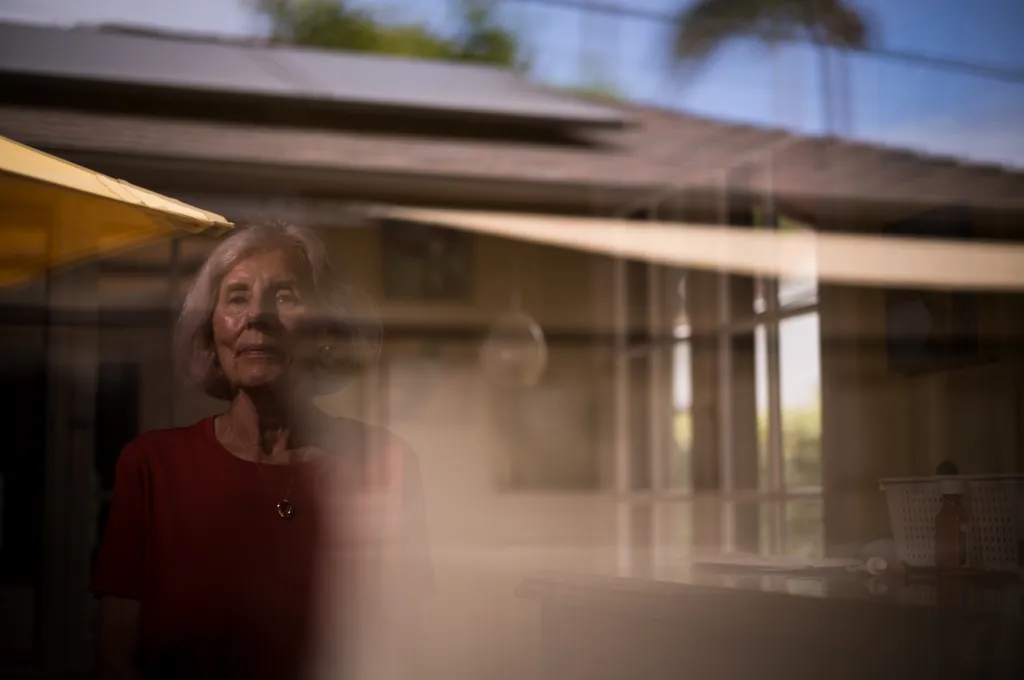 Linda Henry, a woman with gray hair wearing a red shirt, poses for a photo with a reflective background.