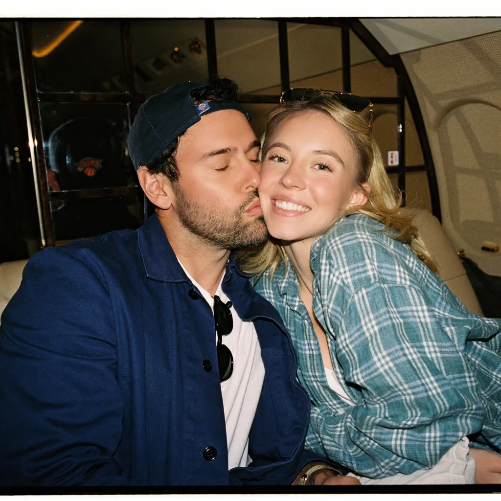 Sydney Sweeney smiling while a man kisses her on the cheek.