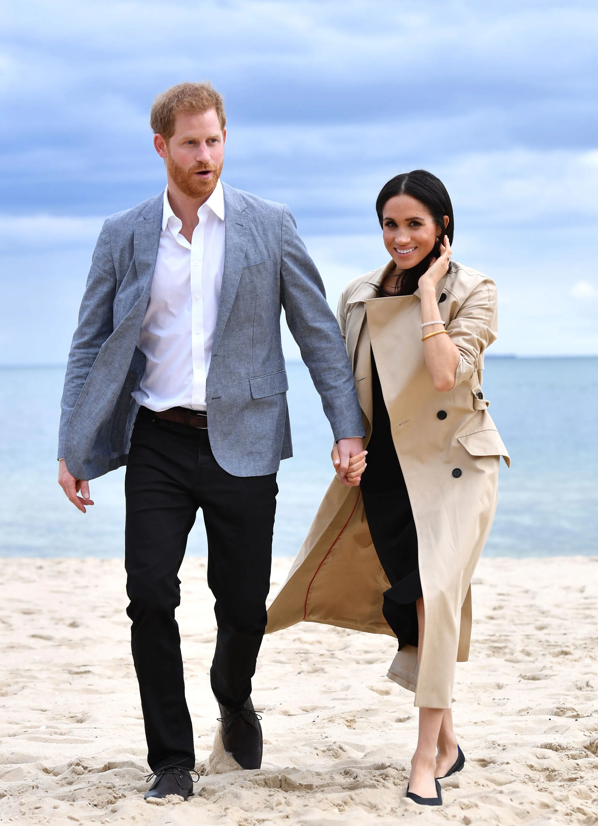 Prince Harry and Meghan Markle holding hands on a sandy beach.