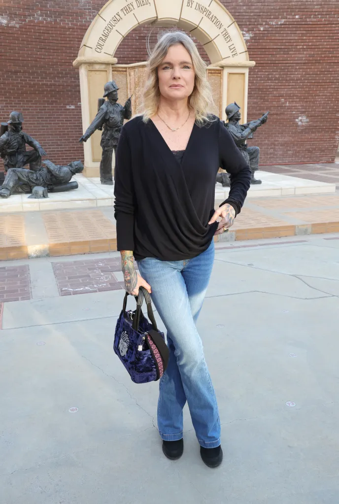Erika Eleniak standing in front of fireman statues at the LA City Fire Museum.