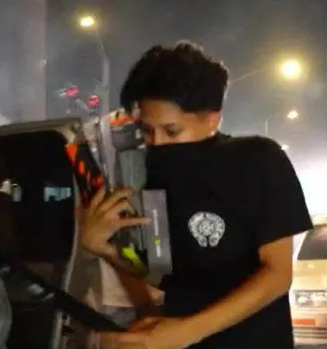 Suspect wearing a black t-shirt with a white graphic on the chest, covering their face with the shirt and holding an item.