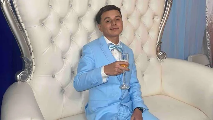 Christopher Garcia, a young man in a light blue suit and bow tie, sitting on an ornate white chair while holding a champagne flute.