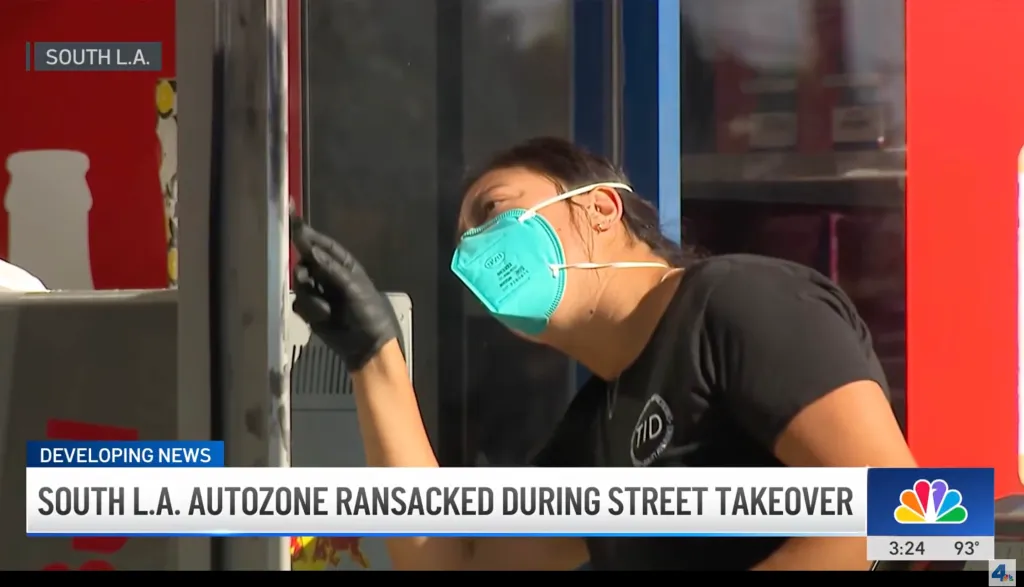 A woman in a face mask and black gloves inspects a damaged store.