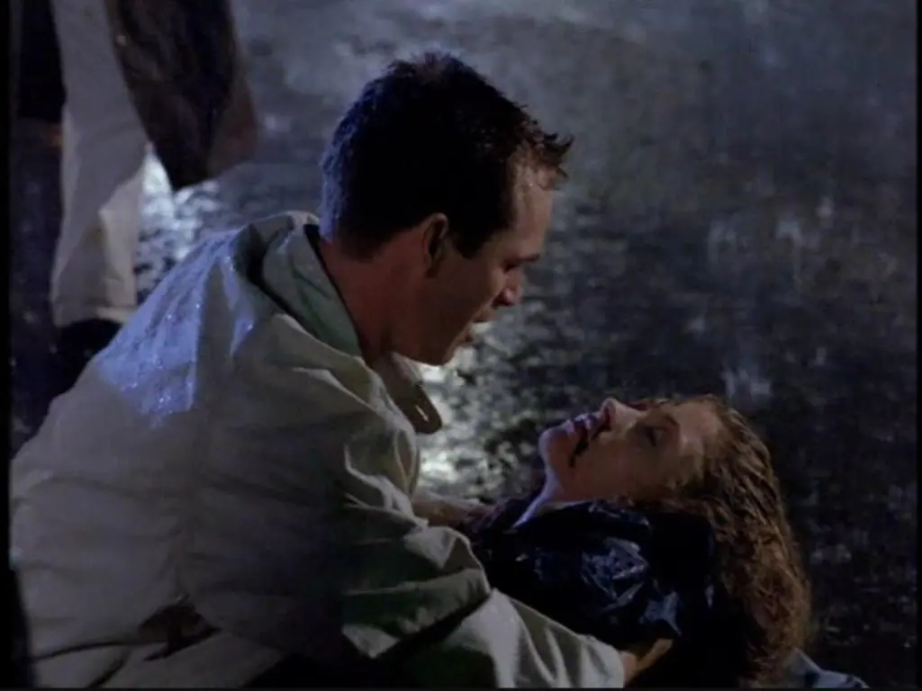 Luke Perry supporting a woman on the ground, both wet from rain.