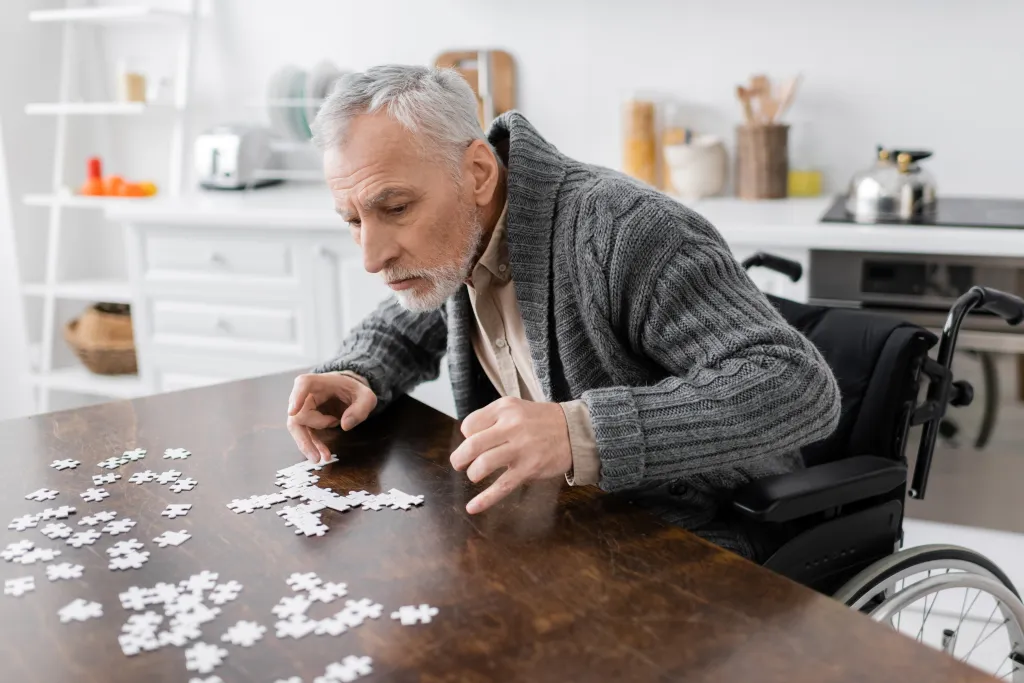 Man with Parkinson's syndrome sitting in a wheelchair and putting together a jigsaw puzzle.