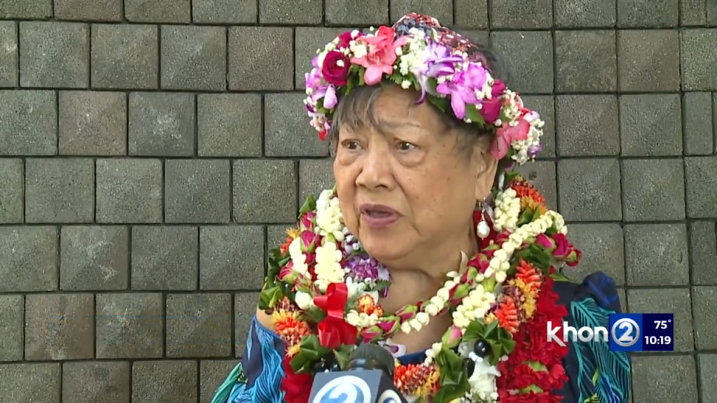 Mary Rivera in an interview, wearing a flower lei and a floral crown.
