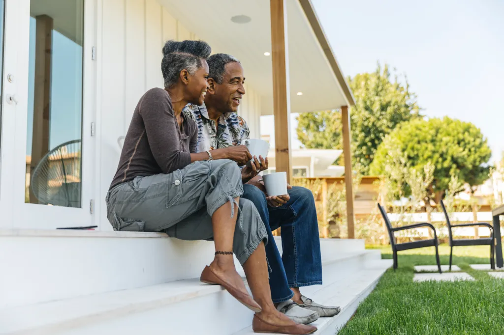A mature couple sits on a porch drinking coffee.