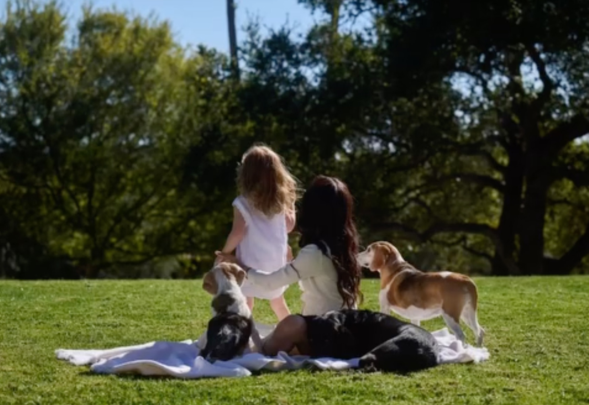 Meghan Markle, her daughter, and three dogs on a lawn.