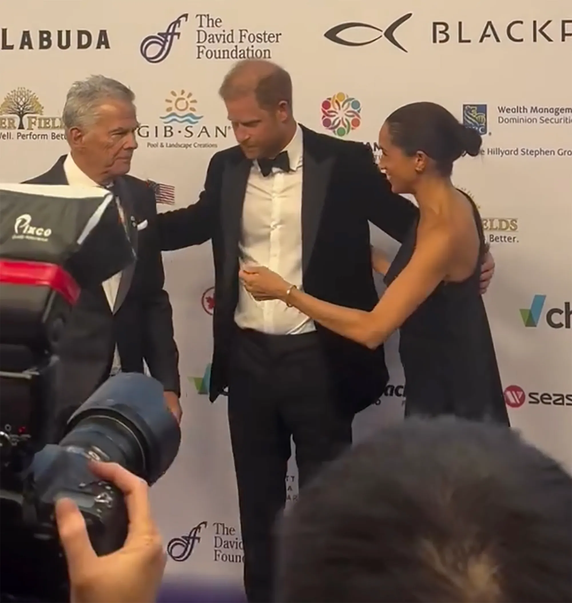 Meghan Markle, Prince Harry, and David Foster posing for a photo.