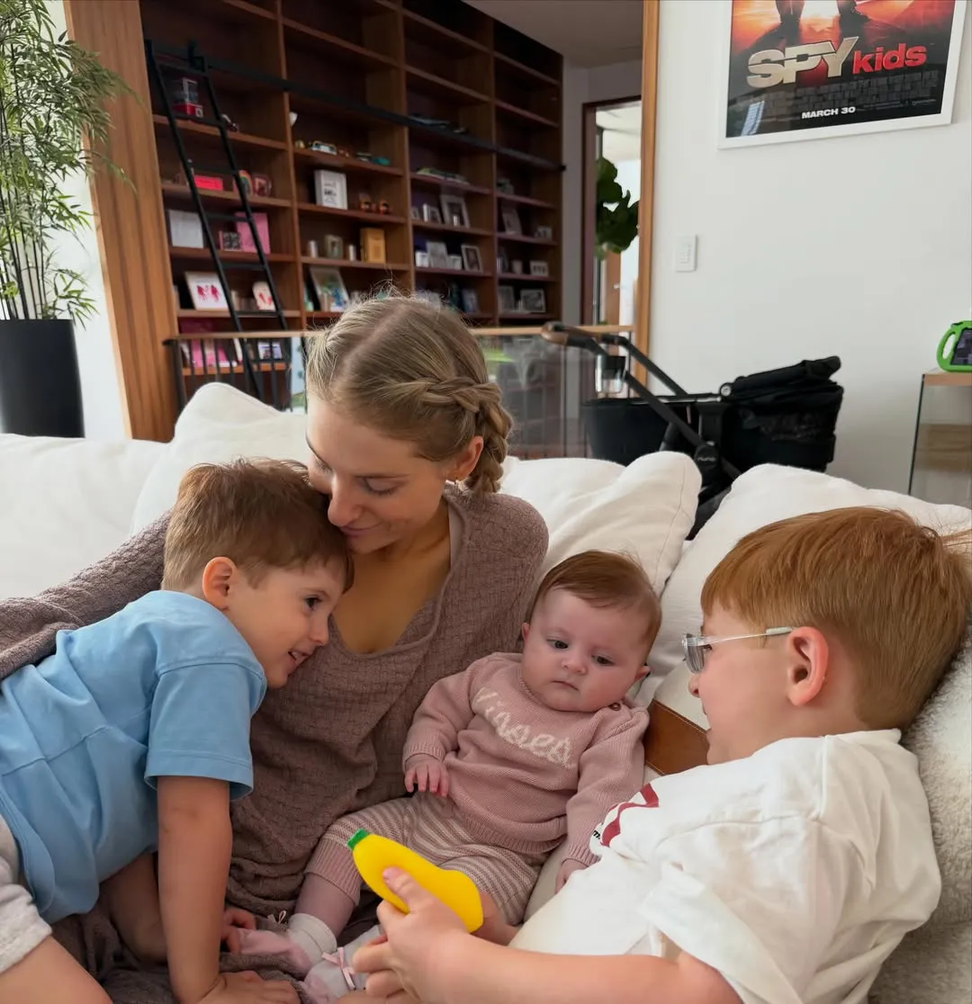 Meghan Trainor and her three children, two boys and one baby girl, sitting on a couch.