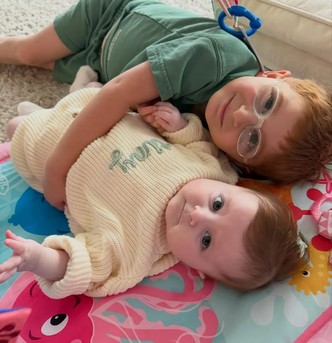 Meghan Trainor's kids, Riley and Mikey, laying on a colorful playmat.