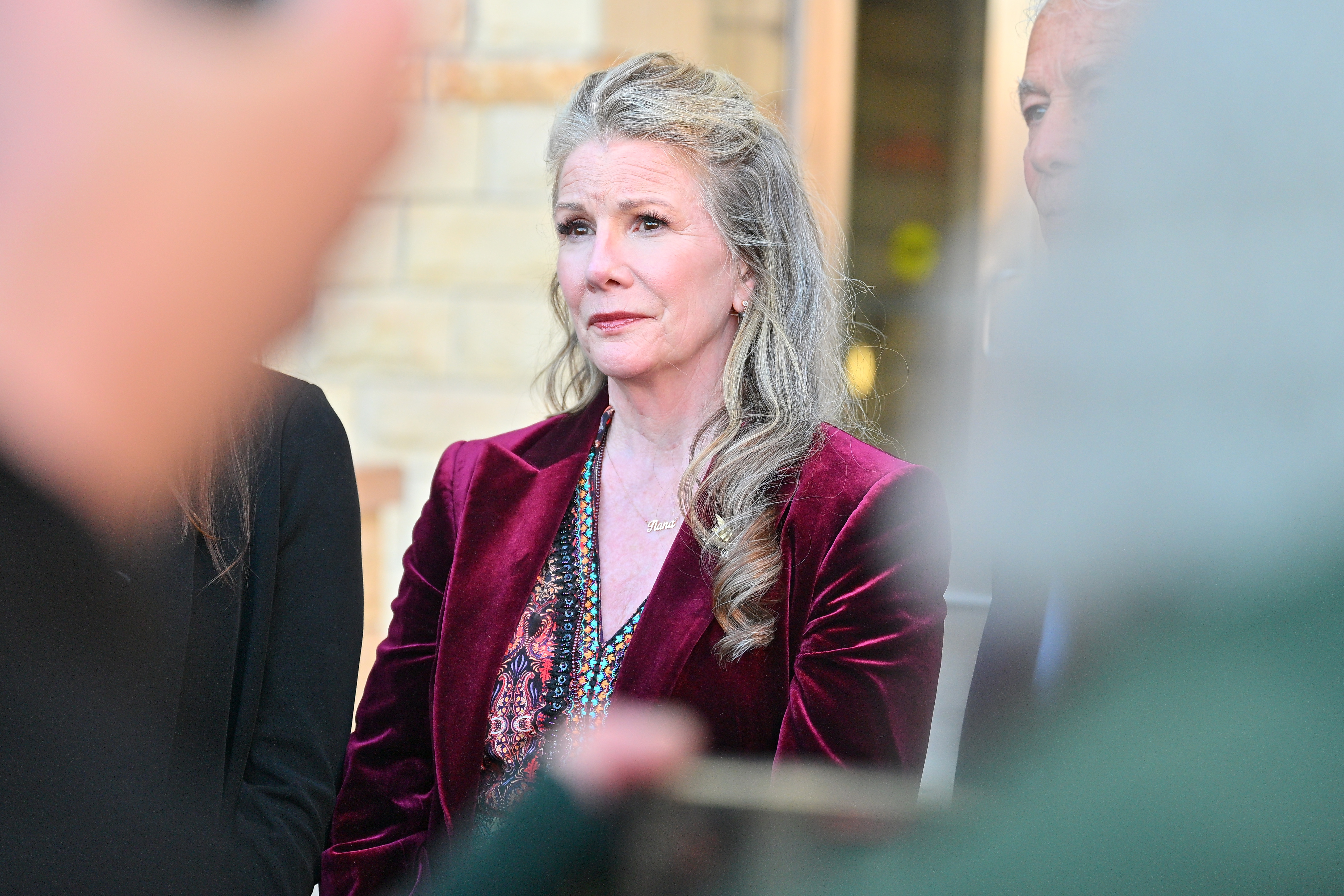 Melissa Gilbert, wearing a burgundy velvet blazer and a colorful top, looking on at a court hearing.