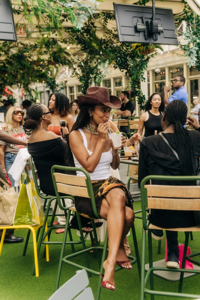 Mia Calabrese wearing a straw hat and gold necklace, sipping a drink at Sadie's Garden Bar.