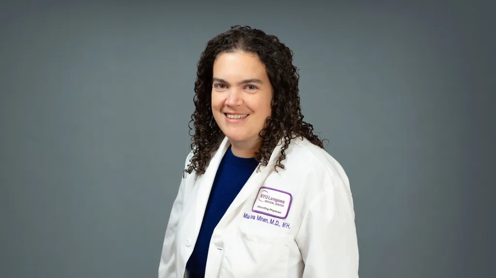 Dr. Mia Minen, a woman with dark curly hair and a white lab coat, smiles at the camera.