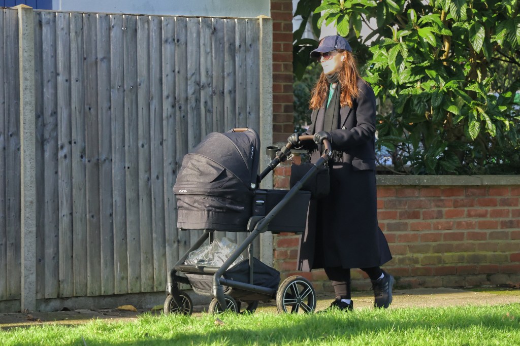 Michelle Dockery pushing a black baby stroller while wearing a dark coat, blue baseball cap, sunglasses, and black gloves.