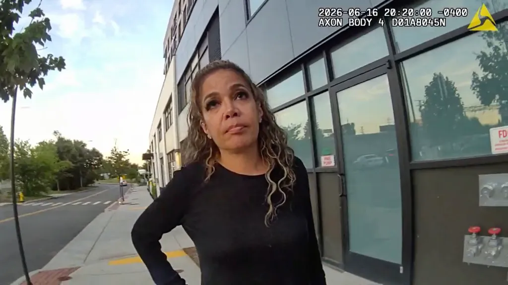 A woman with curly brown hair and a black long-sleeved shirt is seen from a body camera perspective.