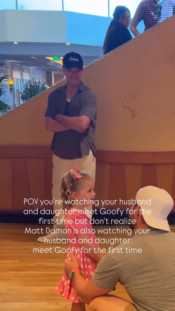 Matt Damon smiles in the background as a father and his young daughter meet Goofy.