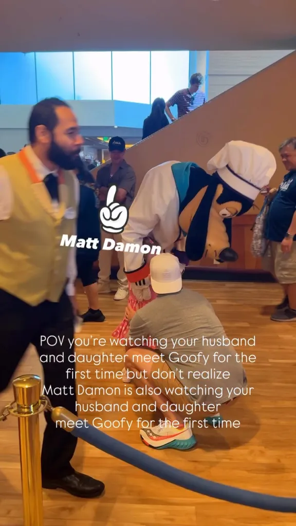 Goofy interacting with a family, while Matt Damon is seen in the background.
