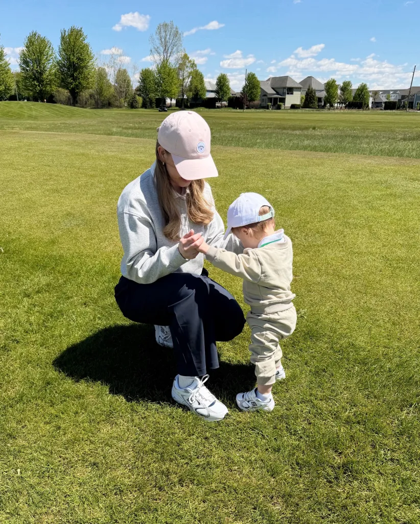A woman in a pink hat holding a toddler's hand on a golf course.