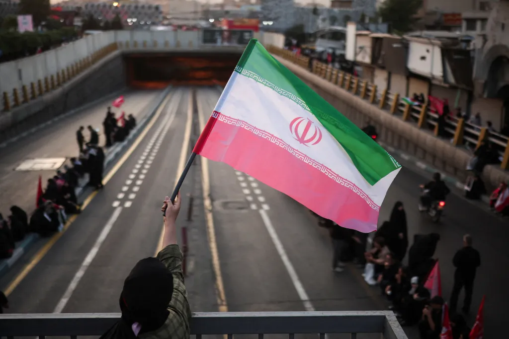 A mourner waves an Iranian flag above a funeral procession.