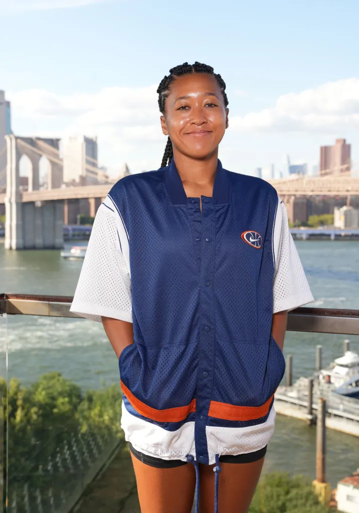 Naomi Osaka smiles in a blue and white jacket overlooking the Brooklyn Bridge.