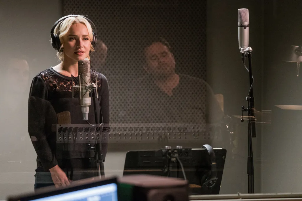 Hayden Panettiere wearing headphones and singing into a microphone in a recording booth.