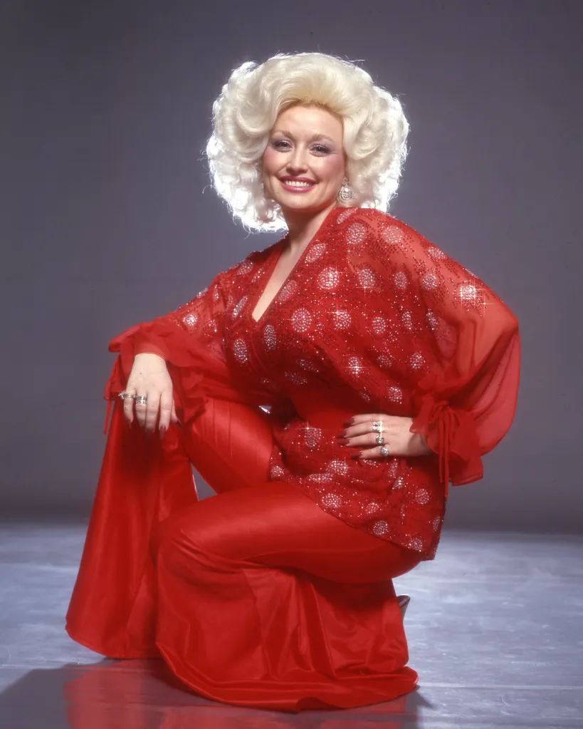 Dolly Parton wearing a sparkly red top and matching pants while crouching.