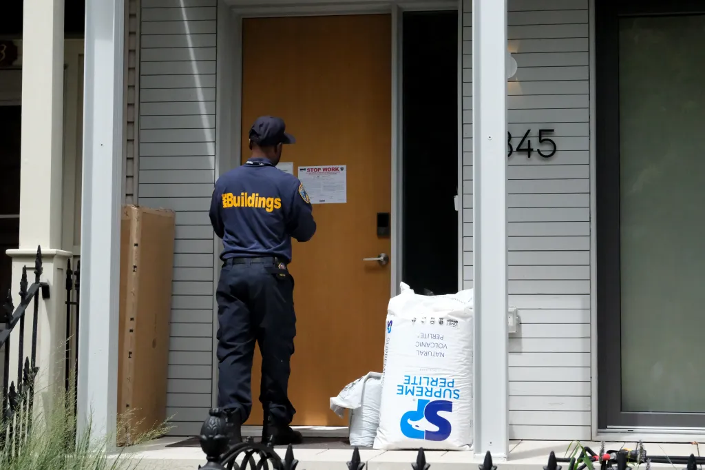 A New York City Department of Buildings inspector posts a stop-work notice on a door.