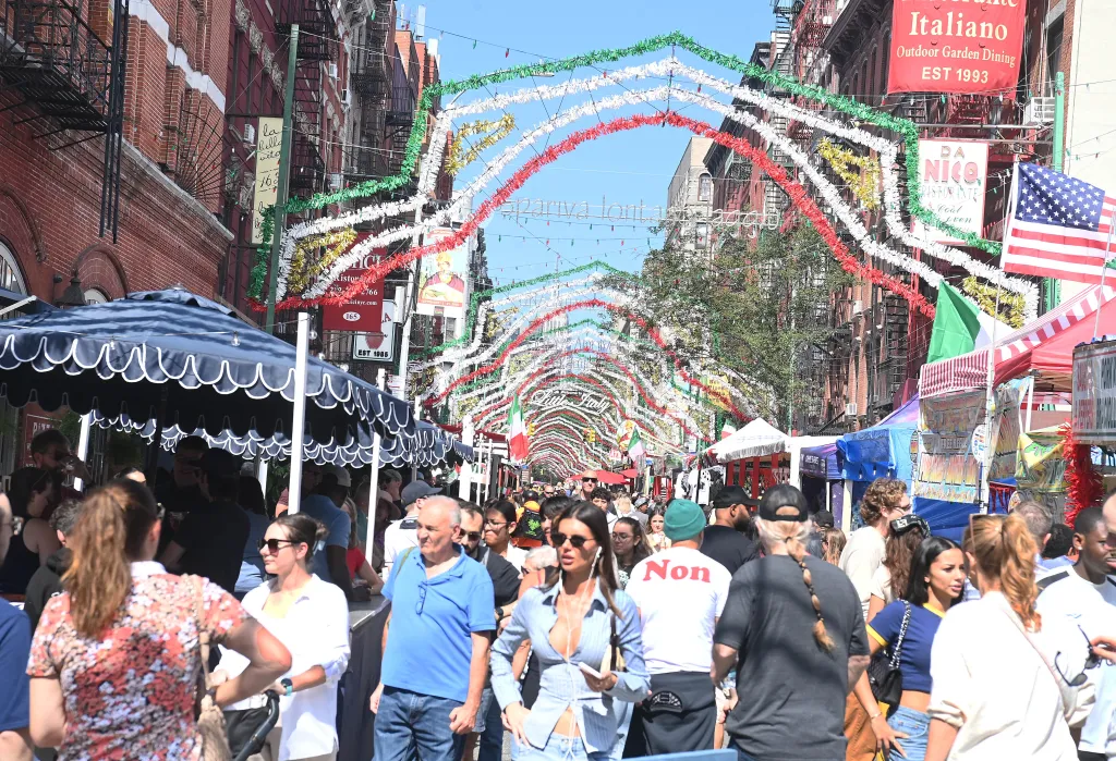 Festival-goers at the Feast of San Gennaro in Little Italy, New York, under festive Italian-themed archways and decorations.