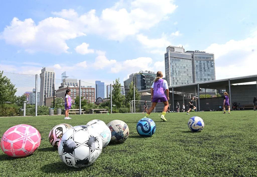 Elementary-aged girls practice soccer on a field in Hudson River Park by the Meatpacking District in New York.