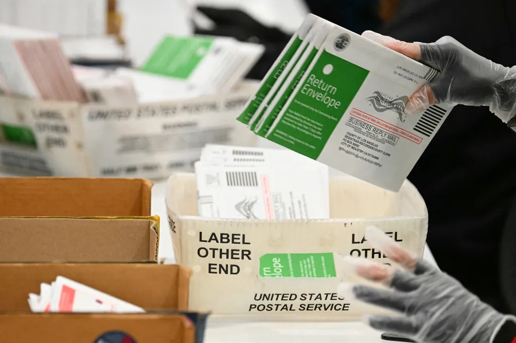 Gloved hands sort through election mail return envelopes.