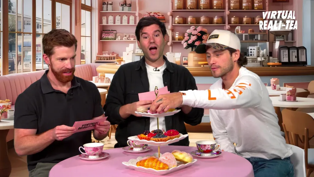Three men sitting at a table with tea and pastries, one holding a pink card that says