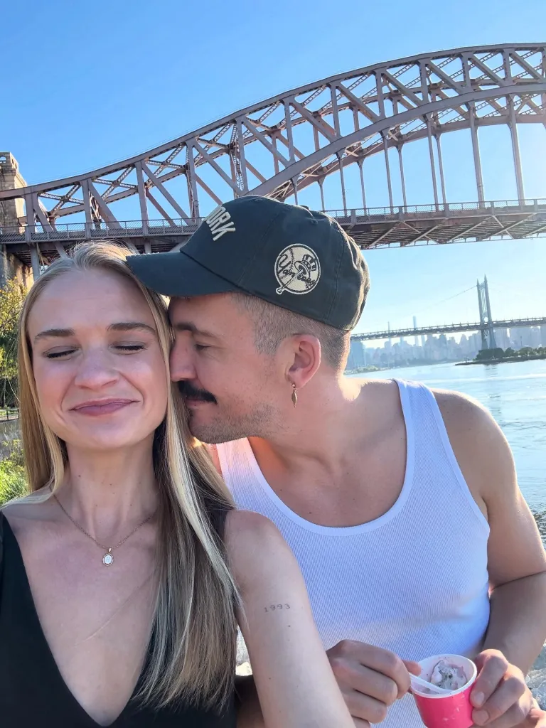 Hannah Alderman and Jason Henley, a couple, pose for a selfie with a bridge in the background.